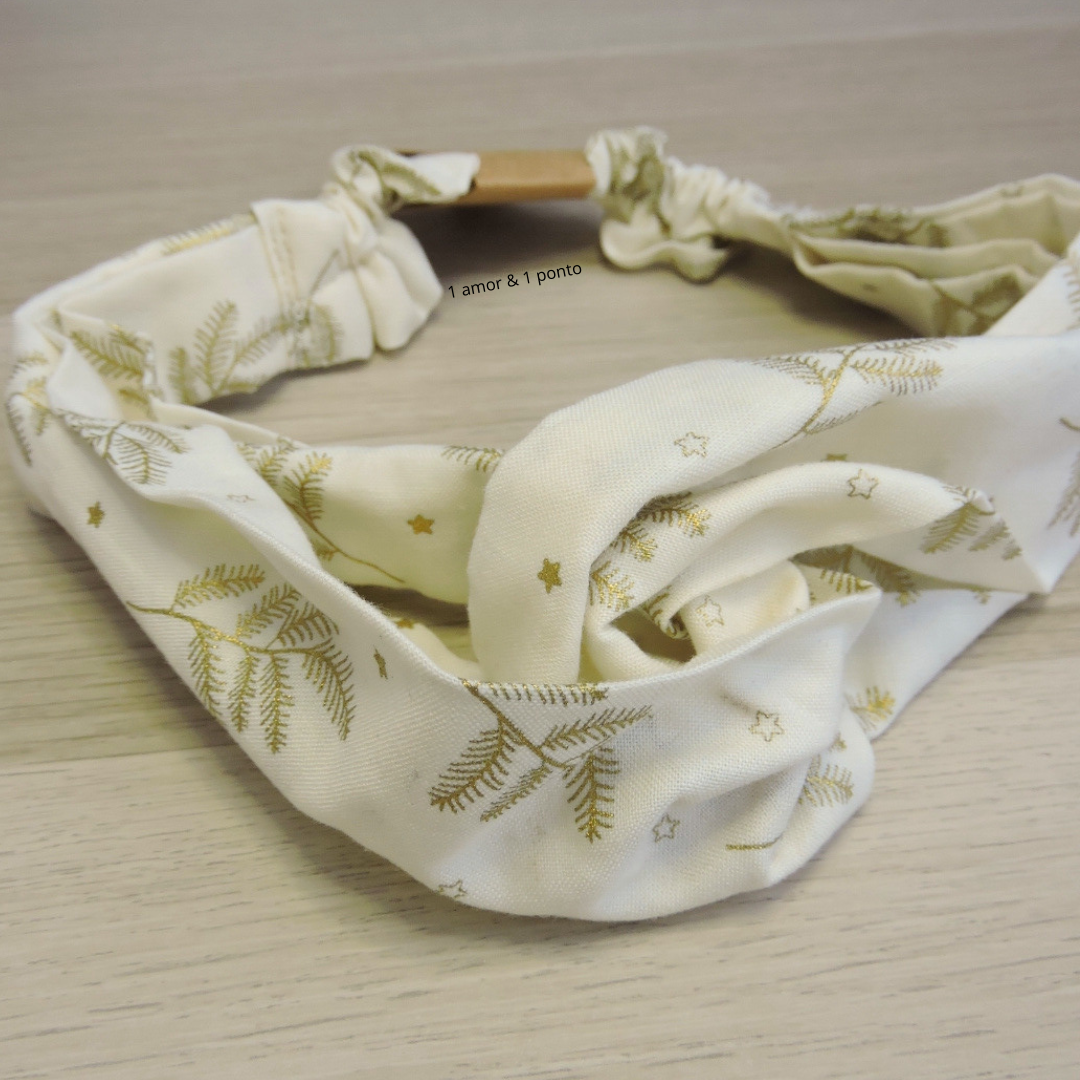 Faixa de cabelo branca com folhas douradas e estrelas, elástica, sobre superfície de madeira