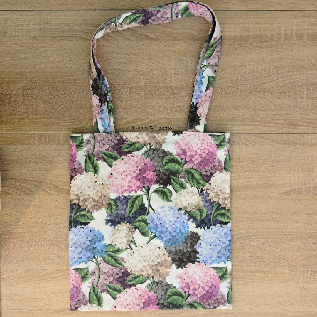 Saco de tecido com padrão floral colorido sobre piso de madeira clara