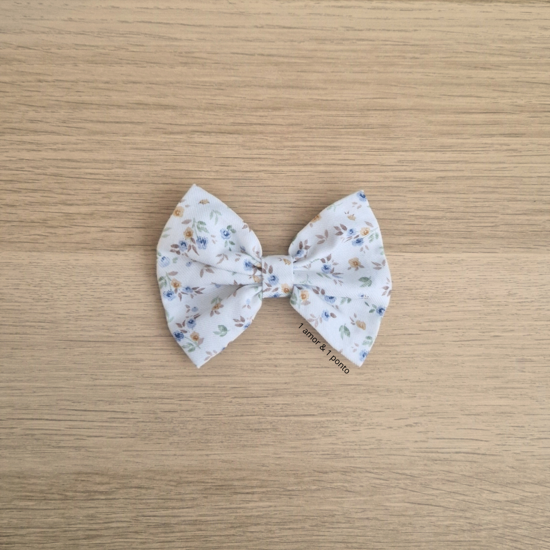 Laço de tecido branco com padrão floral colorido sobre madeira clara