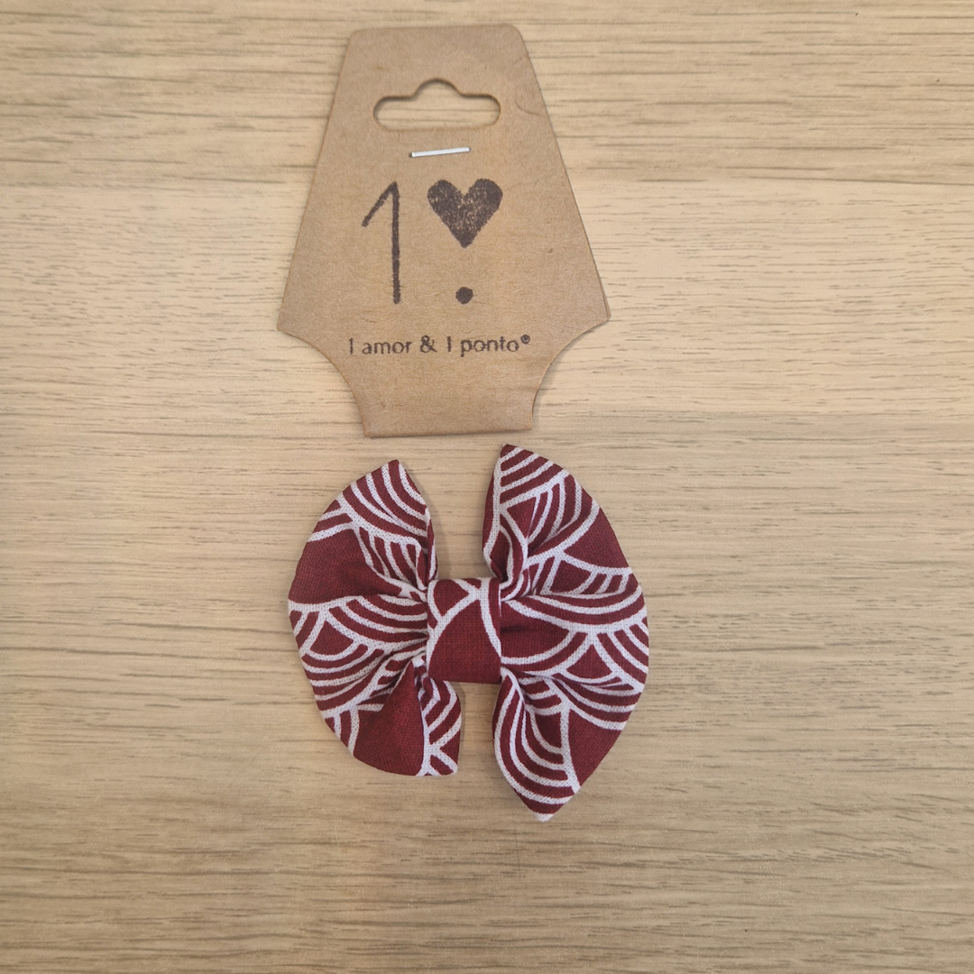 Laço de tecido vermelho com padrão branco e cartão castanho com texto