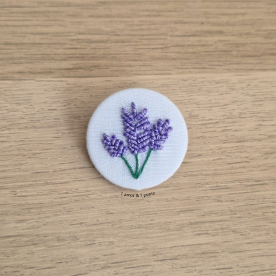 Botão branco bordado com flores roxas sobre madeira clara