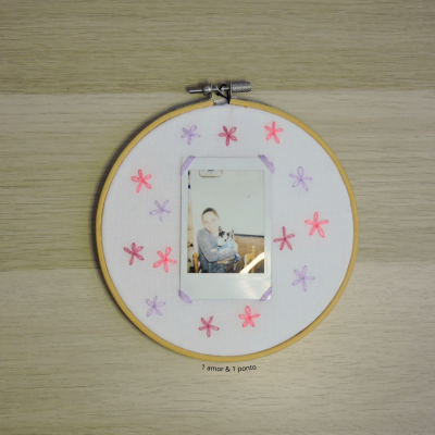 Arco de bordado com tecido branco, flores bordadas rosa e roxo e fotografia instantânea no centro