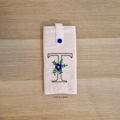 Capa de tecido creme com botão azul e bordado da letra T com flores