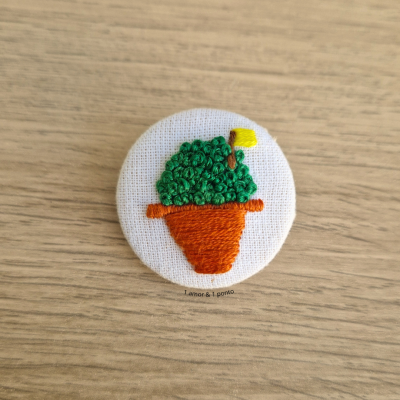 Botão bordado com vaso de planta colorida em tecido branco