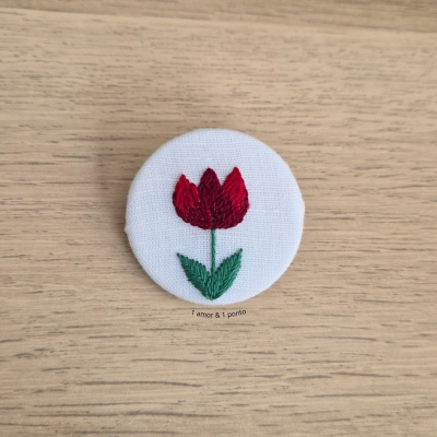 Botão redondo branco com flor bordada vermelha e folhas verdes sobre madeira
