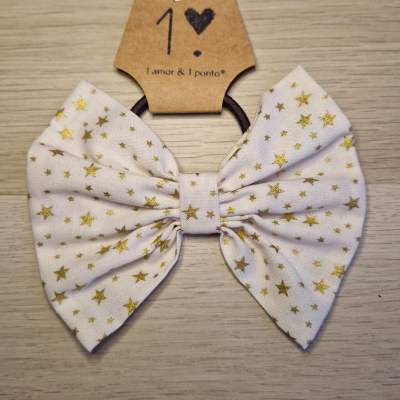 Elástico de cabelo com laço branco e estrelas douradas sobre cartolina castanha