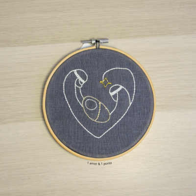 Bordado em bastidor de madeira com desenho abstrato em forma de coração no tecido cinza escuro