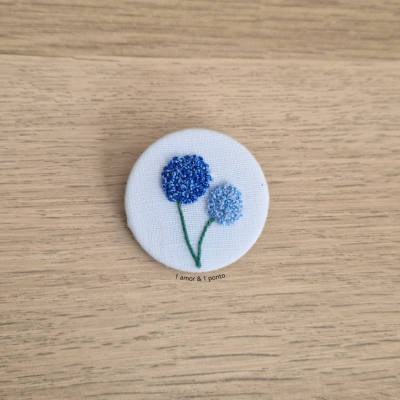 Botão redondo com bordado em flores azuis e texto em tecido branco