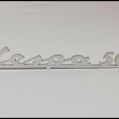 Emblema metálico prateado com texto Vespa 50 em estilo cursivo