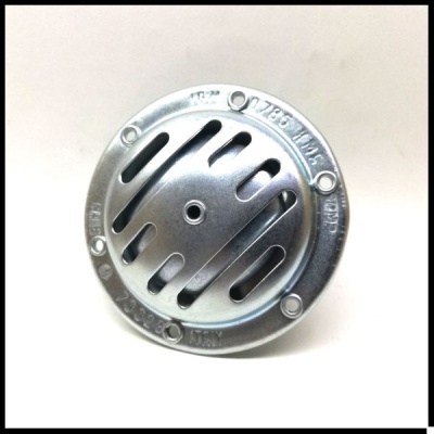 Peça metálica redonda prateada com aberturas e inscrições visíveis.