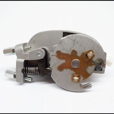 Peça metálica com mola e parafusos, com sinais de ferrugem, sobre fundo branco