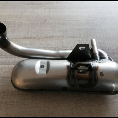 Escapamento automóvel em metal prateado com tubo curvo e suporte preto sobre mesa de madeira clara