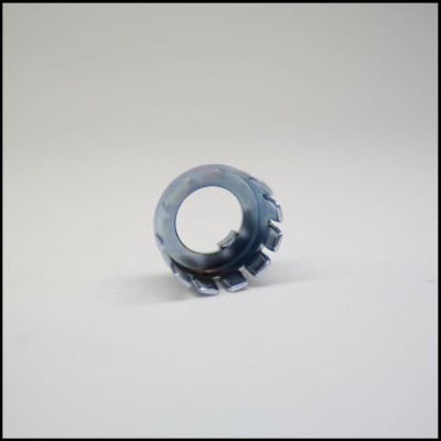 Anel metálico cinzento com dentes salientes numa superfície branca