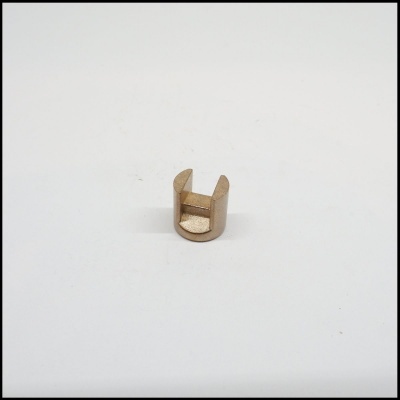 Pequena peça metálica dourada cilíndrica com secção aberta sobre fundo branco