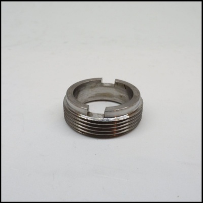 Anel metálico prateado com roscas e entalhes sobre superfície branca