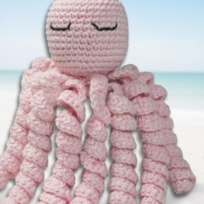 Polvo de croché cor-de-rosa com tentáculos enrolados e olhos fechados