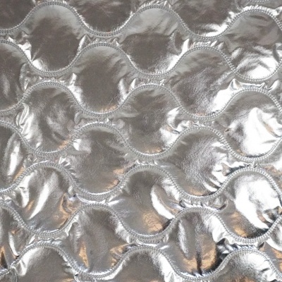 Superfície acolchoada prateada com textura ondulada e relevo em bolhas.