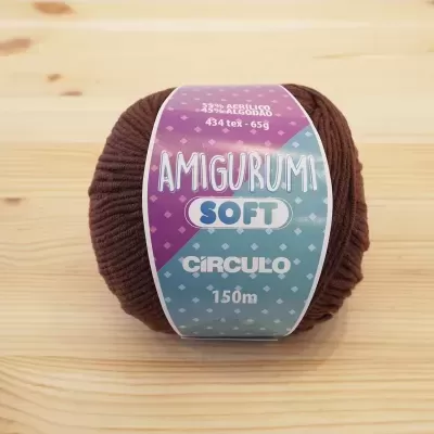 Novelo de fio castanho escuro com rótulo colorido sobre madeira clara