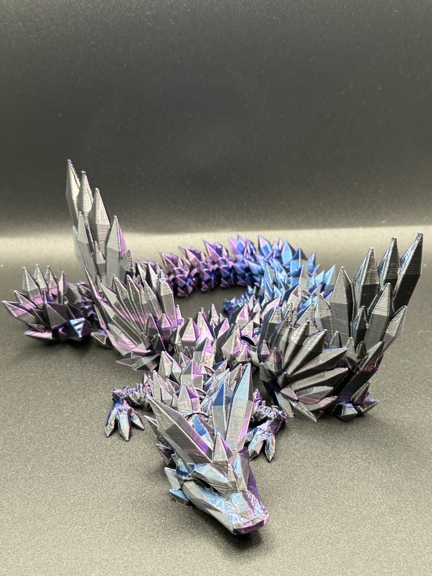 Dragão decorativo preto com picos triangulares metálicos em roxo e azul