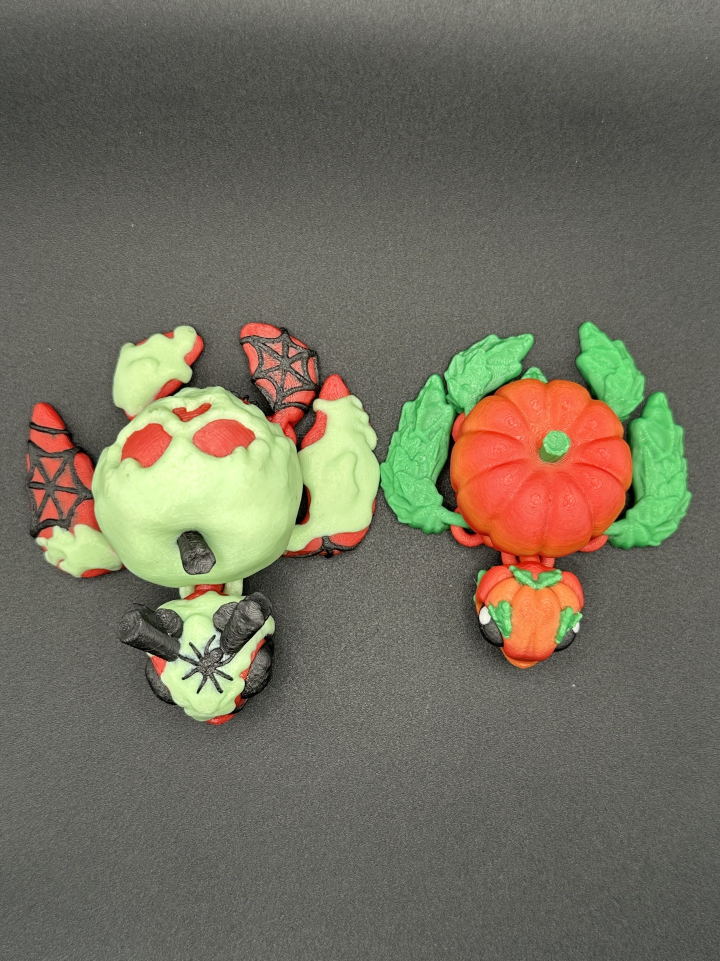 Duas figuras pequenas em borracha ou plástico com motivos de Halloween, uma verde com vermelho e outra laranja com verde.
