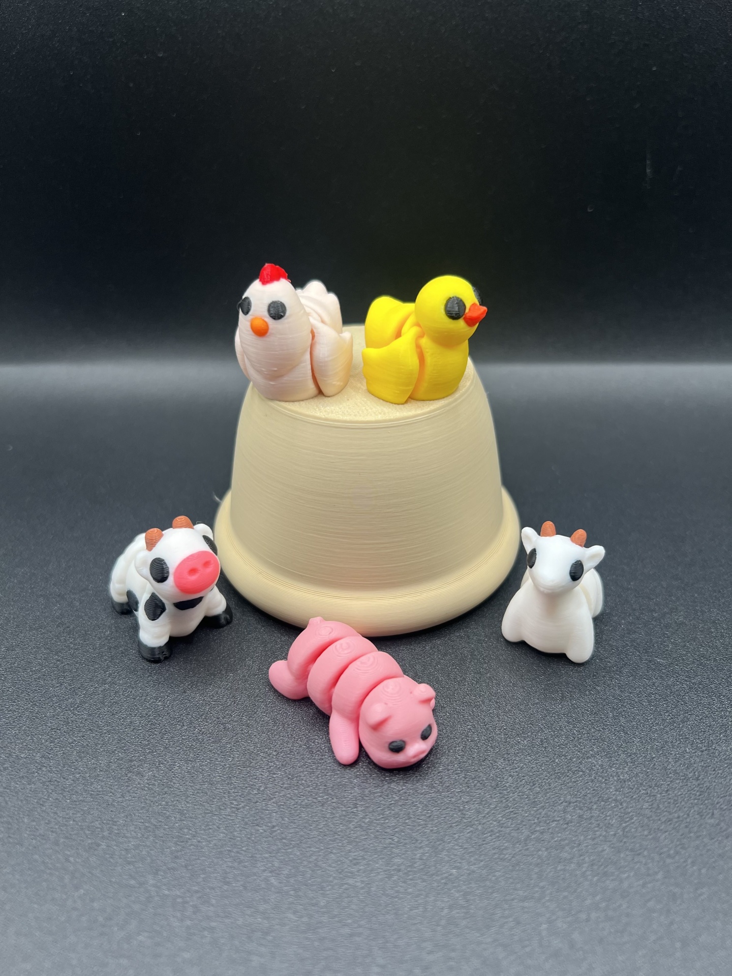Miniaturas de animais feitas de massa para modelar em torno de um vaso bege sobre fundo preto