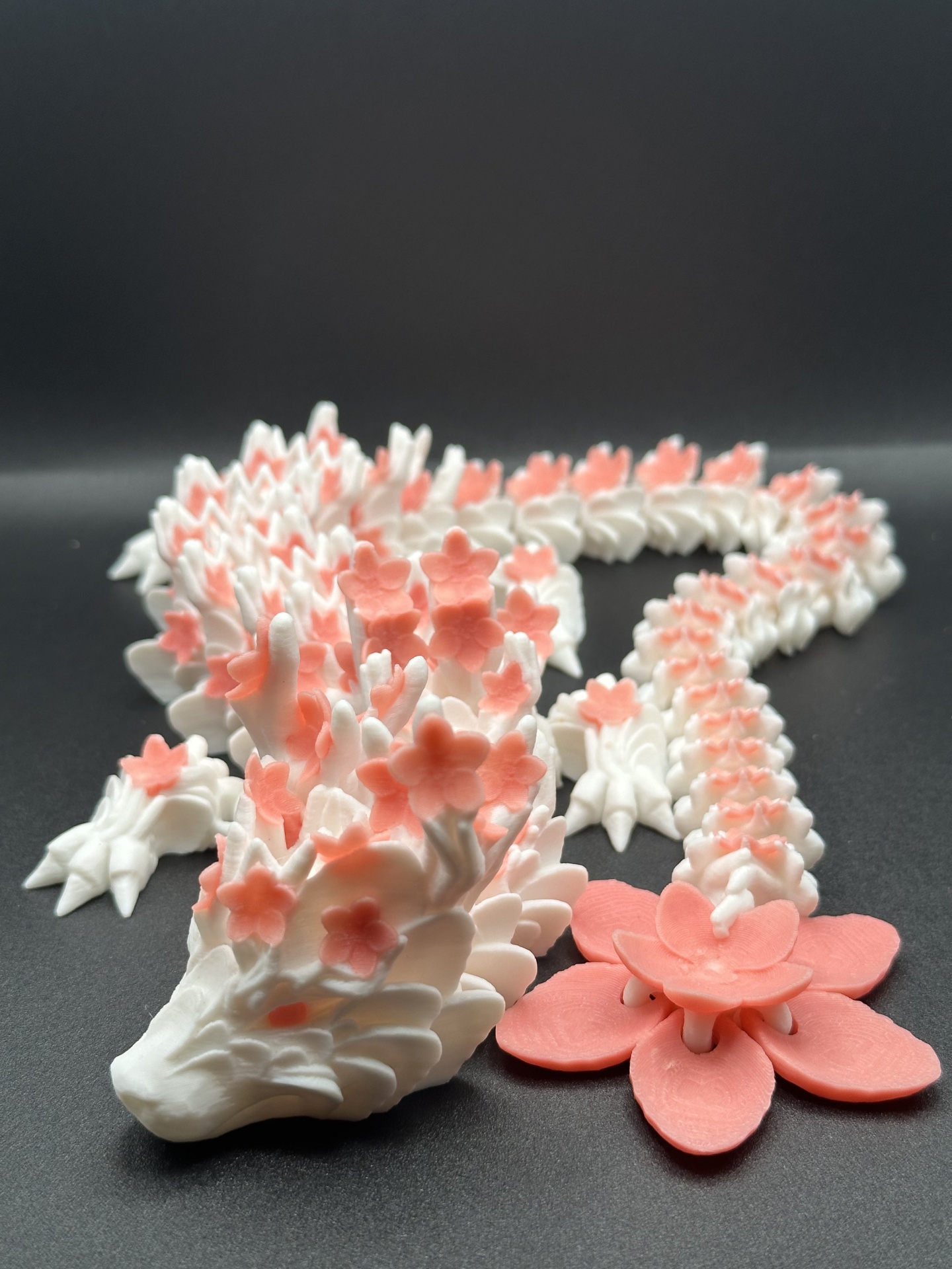 Escultura de dragão branco com flores cor-de-rosa em fundo preto