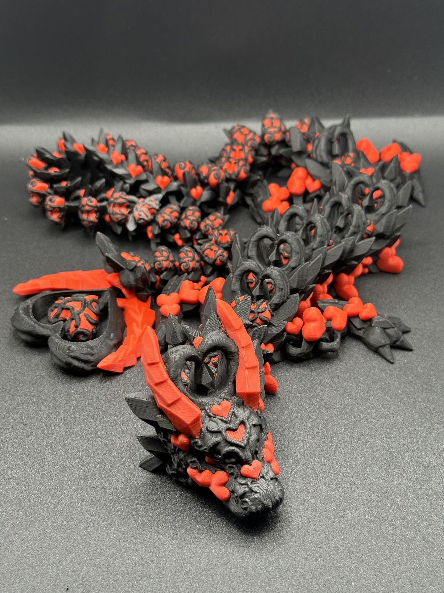 Escultura de dragão preta e vermelha com corações e chifres em fundo preto