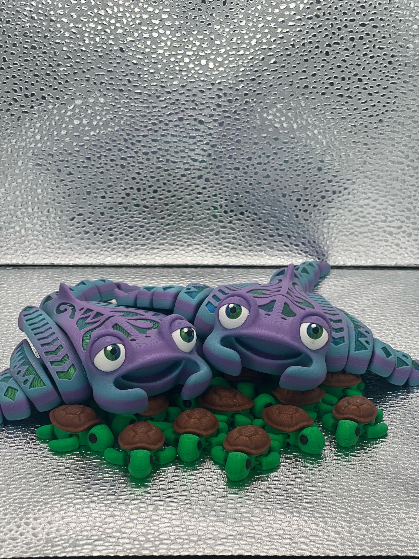 Estatuetas de tartarugas roxas com padrões azuis e miniaturas verdes de tartarugas sobre fundo prateado