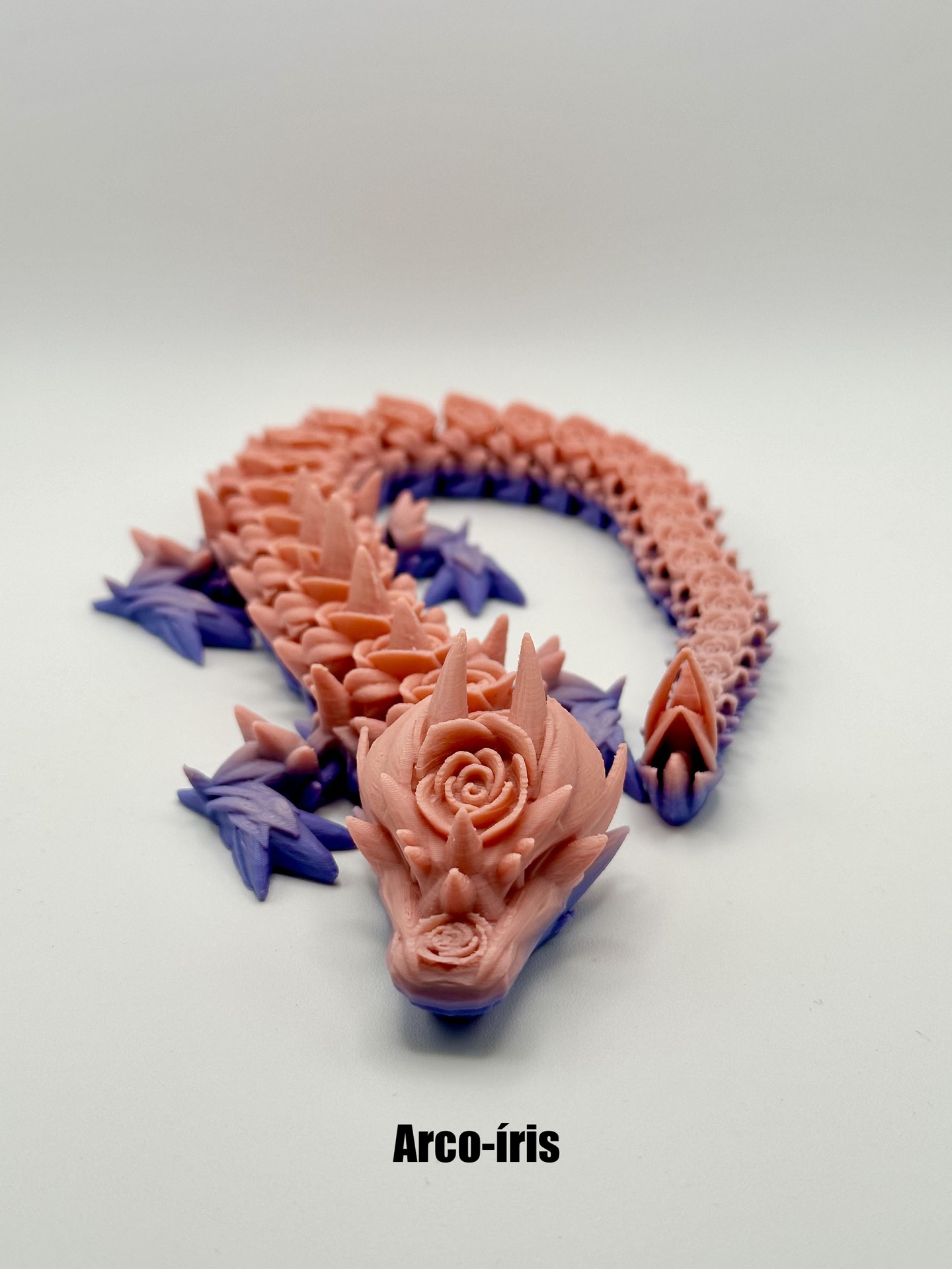 Escultura de dragão rosa com detalhes roxos e texto 'Arco-íris'