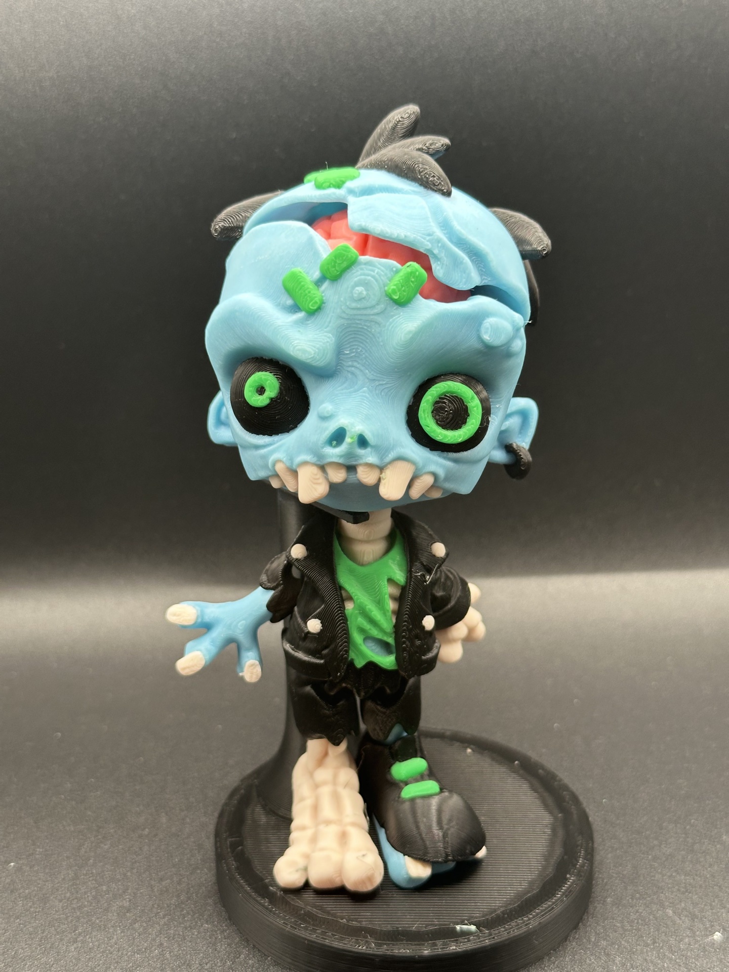 Figura colecionável de zumbi azul com roupa preta e verde em suporte preto