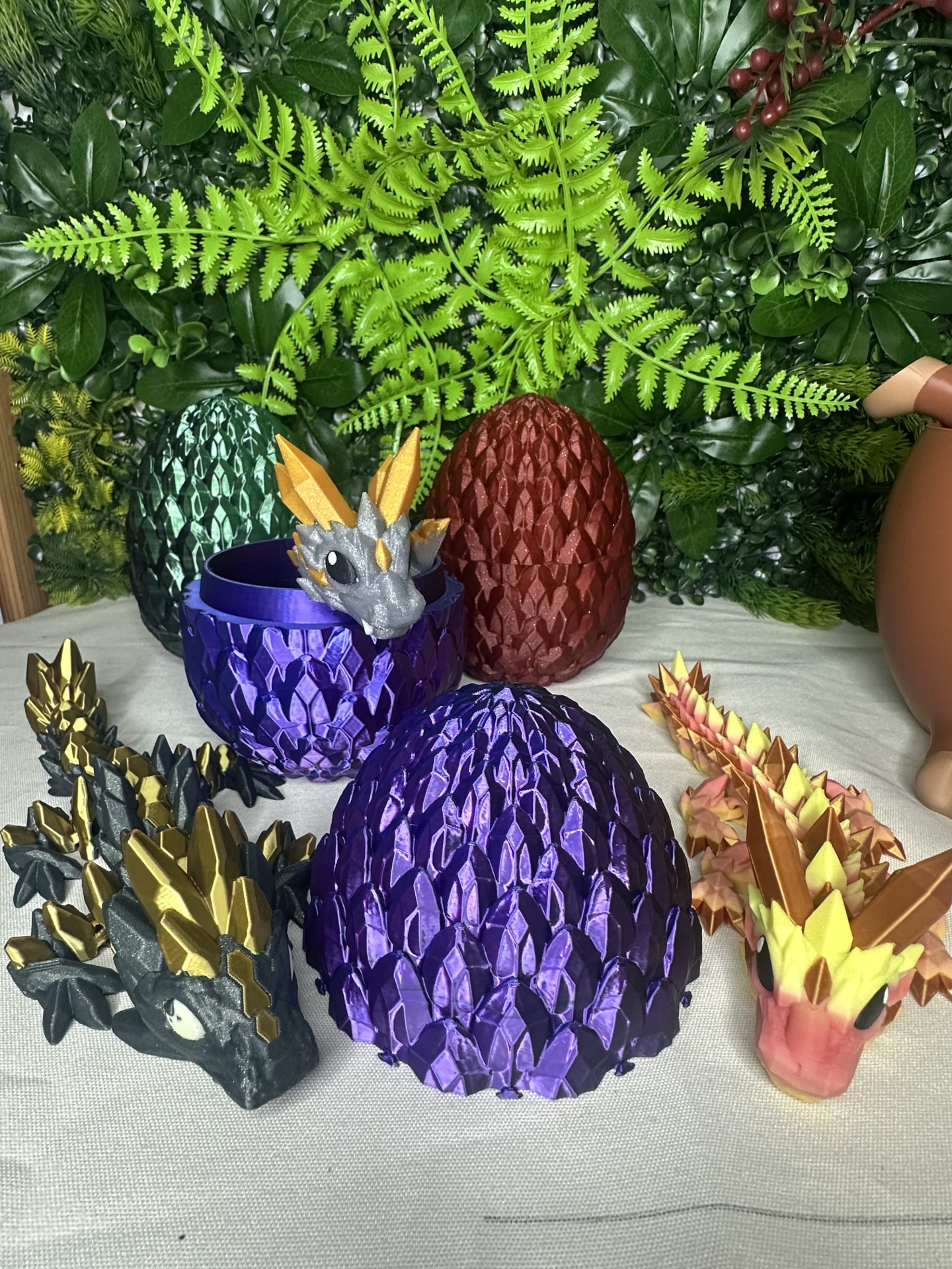 Figuras e ovos de dragão em plástico colorido sobre tecido branco com fundo de folhas artificiais