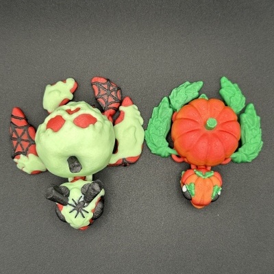 Duas figuras pequenas em borracha ou plástico com motivos de Halloween, uma verde com vermelho e outra laranja com verde.