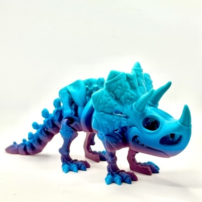 Boneco dinossauro azul e roxo com três chifres sobre fundo branco