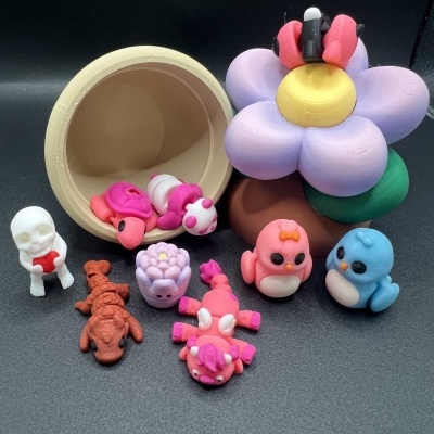 Brinquedos coloridos de borracha incluindo flor grande, caneca e figuras de animais sobre fundo preto.