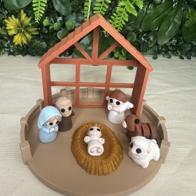 Miniatura presépio de Natal em plástico com manjedoura, figuras e estábulo castanho sobre mesa clara