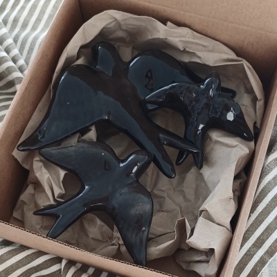 Três figuras decorativas de pássaros pretos de cerâmica numa caixa de cartão