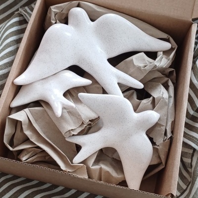 Três pássaros decorativos brancos em cerâmica dentro de uma caixa de papelão com papel kraft