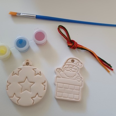Enfeites natalícios em argila para pintar com pincel e tintas amarelo, azul e rosa sobre fundo branco.