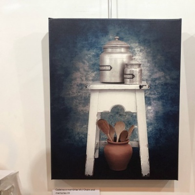 Pintura de uma mesa branca com panela de metal e vaso com colheres de pau