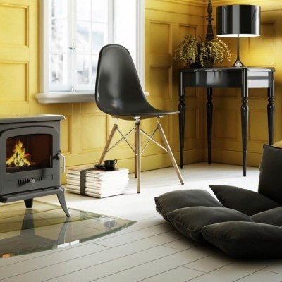 Sala com cadeira preta, lareira a lenha, mesa de apoio, sofá cinzento e paredes amarelas