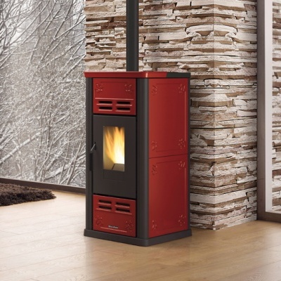Estufa vermelha e preta com fogo aceso numa sala com chão de madeira e paredes de pedra