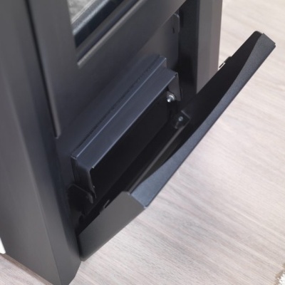 Porta de metal preto aberta parcialmente com compartimento interno, sobre chão de madeira claro e tapete branco ao lado.