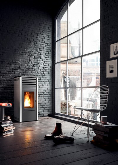 Sala moderna com lareira acesa e cadeira aramada junto a uma grande janela.