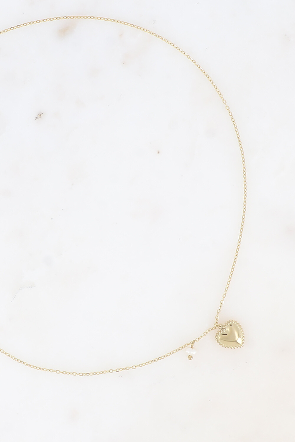 FIO NEREA Colar dourado com pendente de coração e pérola sobre superfície branca