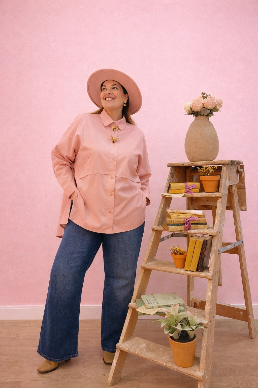 CAMISA PAULA ROSA Mulher com roupa rosa e azul junto a escada de madeira com livros e vasos