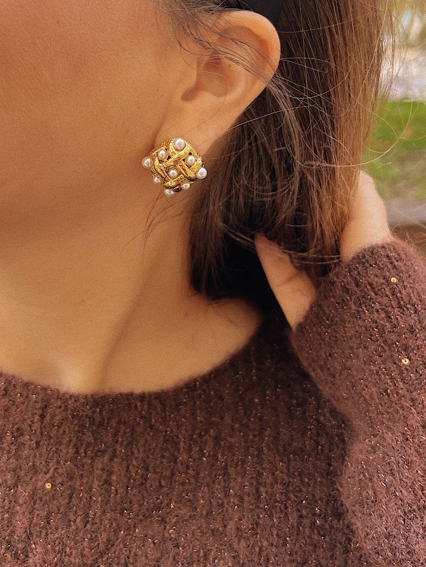 BRINCOS NENÉ Brinco dourado com pérolas usado por pessoa com pulôver castanho