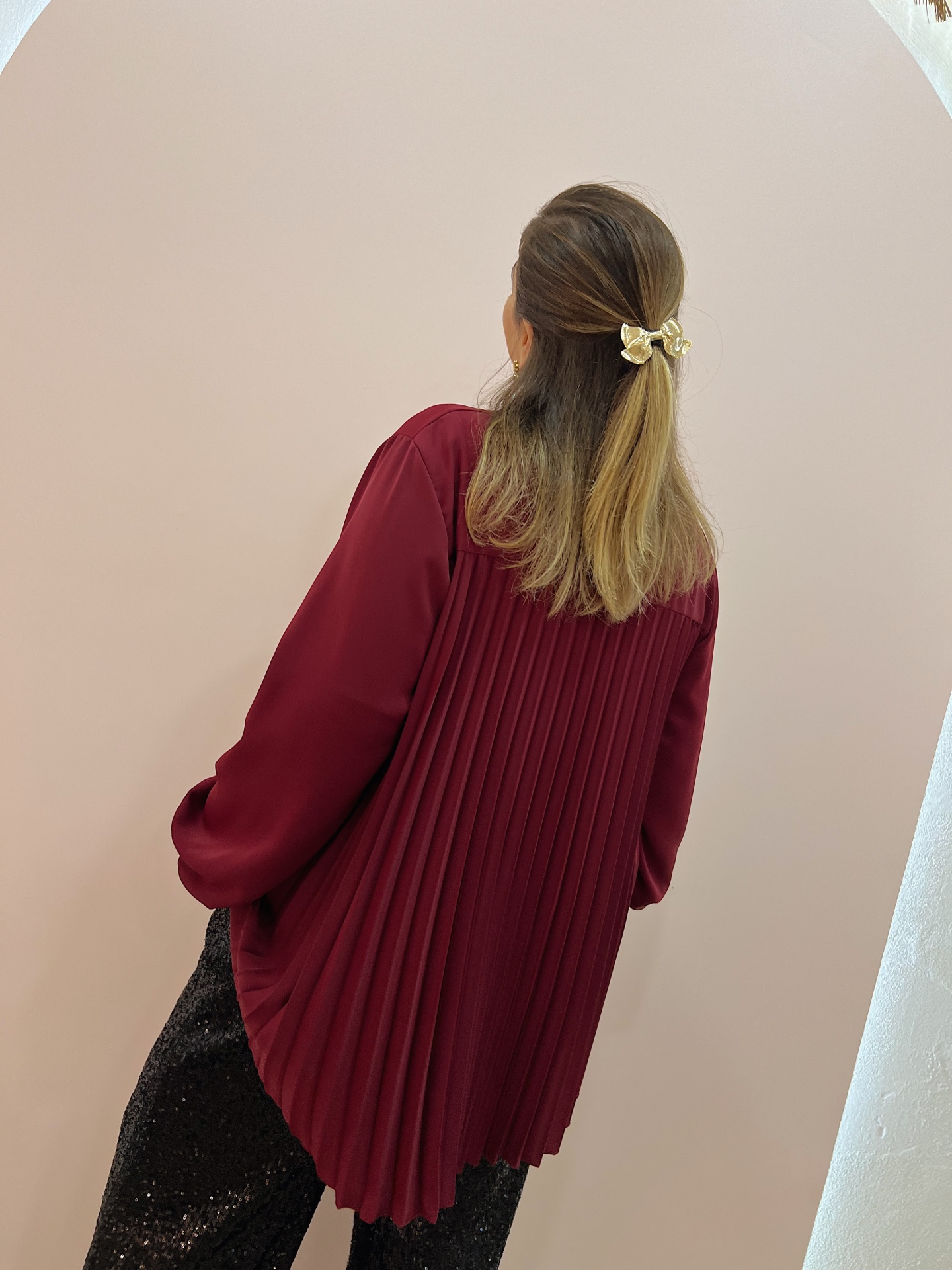 CAMISA NANETE Blusa vinho plissada com calças pretas brilhantes e laço dourado no cabelo