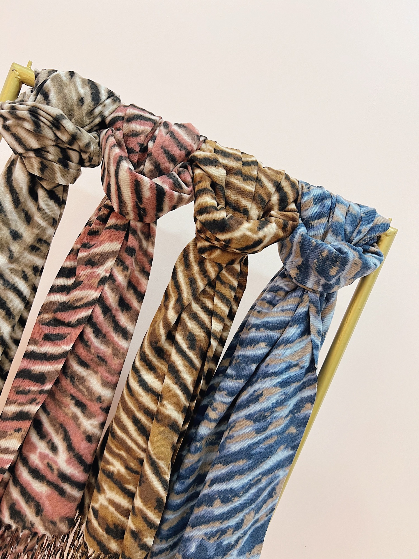 ECHARPE NAMI Quatro cachecóis com padrão animal em várias cores pendurados num suporte dourado.