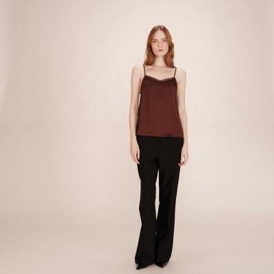 Mulher com top cetim castanho com renda e calças pretas numa pose frontal