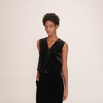 Mulher a usar colete preto de veludo e calças pretas em fundo bege claro